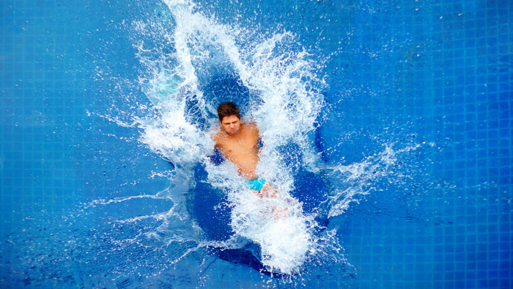 Ein Teenager springt ins Becken und versucht viel Wasser zu spritzen